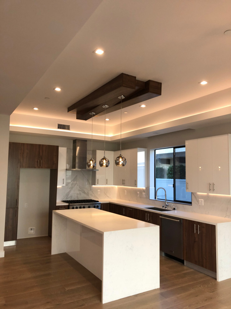 Mid-sized modern l-shaped eat-in kitchen in Los Angeles with a single-bowl sink, flat-panel cabinets, dark wood cabinets, quartzite benchtops, white splashback, porcelain splashback, medium hardwood floors, with island, brown floor and white benchtop.