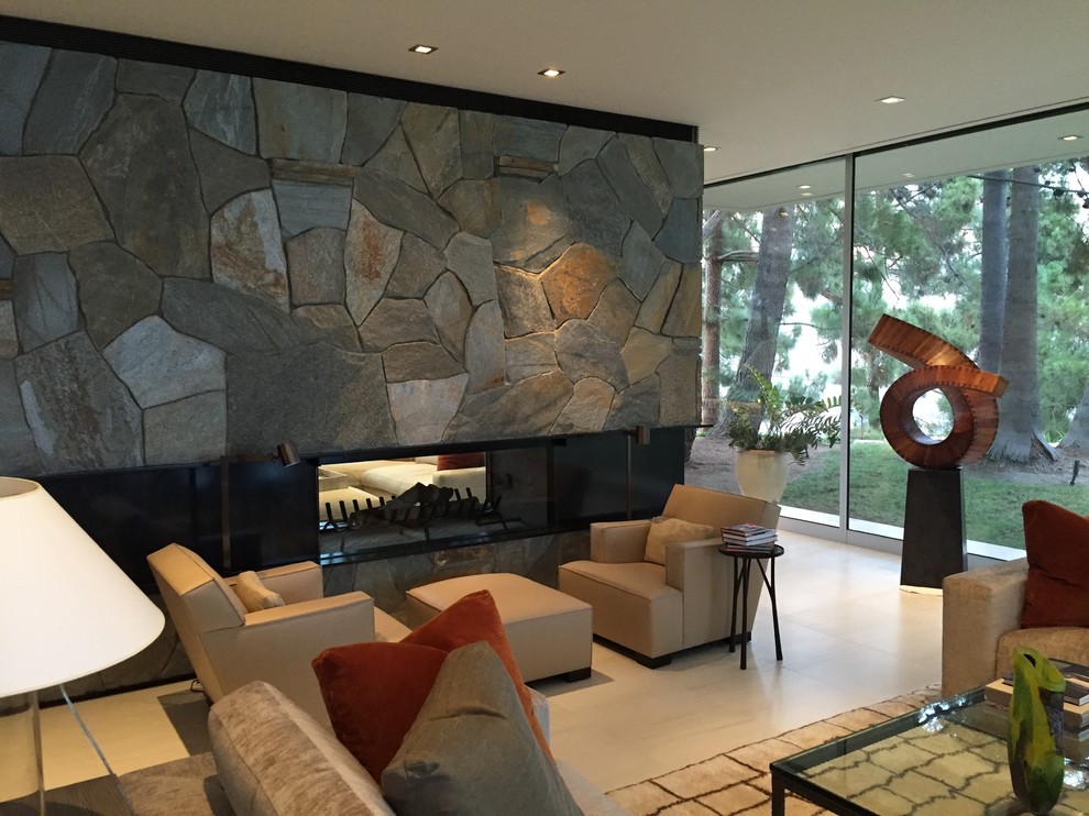 Photo of a mid-sized midcentury open concept living room in Los Angeles with beige walls, porcelain floors, a two-sided fireplace, a stone fireplace surround and beige floor.