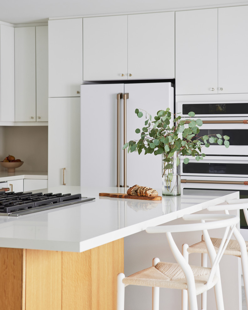 Example of a large 1950s u-shaped light wood floor and beige floor open concept kitchen design in Los Angeles with an undermount sink, flat-panel cabinets, white cabinets, quartz countertops, white backsplash, quartz backsplash, white appliances, an island and white countertops