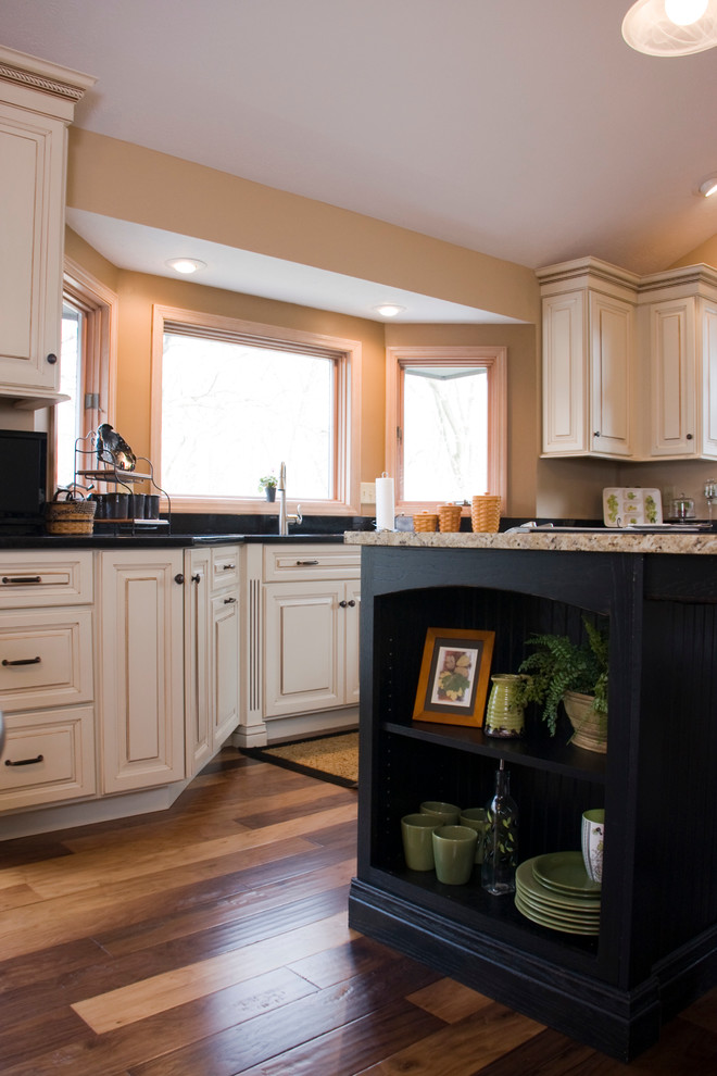 Example of a large transitional l-shaped medium tone wood floor eat-in kitchen design with an undermount sink, raised-panel cabinets, distressed cabinets, granite countertops, black backsplash, stainless steel appliances and an island