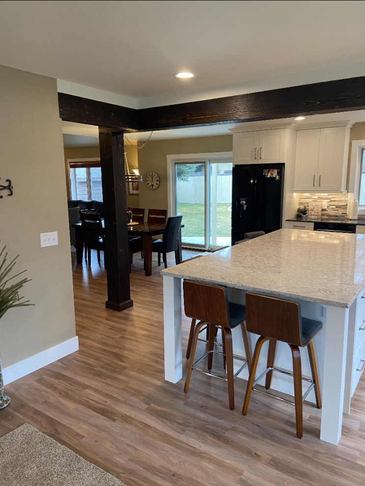 Example of a mid-sized transitional single-wall vinyl floor and multicolored floor eat-in kitchen design with an undermount sink, shaker cabinets, white cabinets, quartz countertops, multicolored backsplash, metal backsplash, black appliances, an island and white countertops