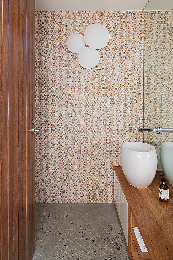 This is an example of a contemporary powder room in Melbourne with a vessel sink, flat-panel cabinets, medium wood cabinets, wood benchtops, beige tile, mosaic tile, concrete floors and brown benchtops.