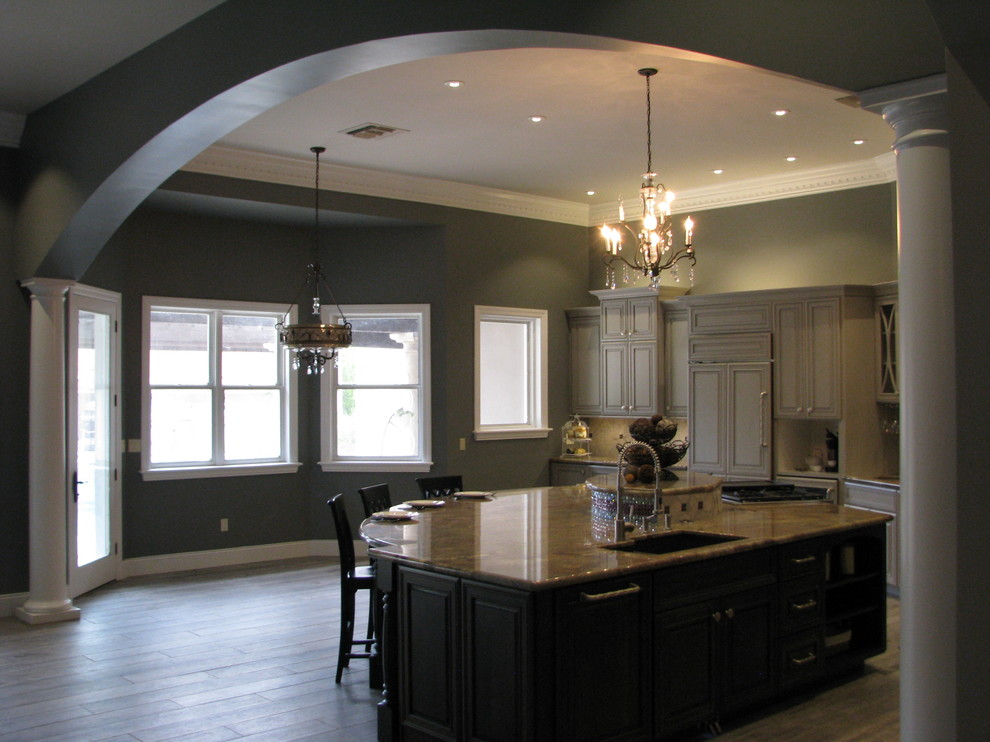 Huge transitional l-shaped porcelain tile open concept kitchen photo with an undermount sink, raised-panel cabinets, gray cabinets, granite countertops, gray backsplash, stone tile backsplash, stainless steel appliances and an island