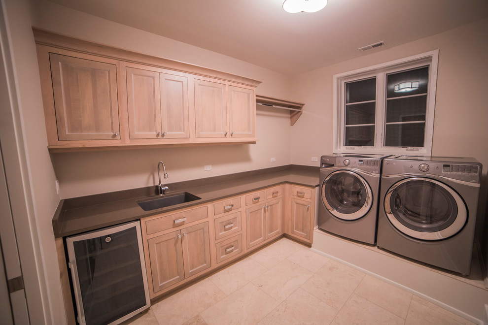 Large transitional l-shaped dedicated laundry room in Chicago with an undermount sink, flat-panel cabinets, light wood cabinets, quartzite benchtops, beige walls, travertine floors and a side-by-side washer and dryer.