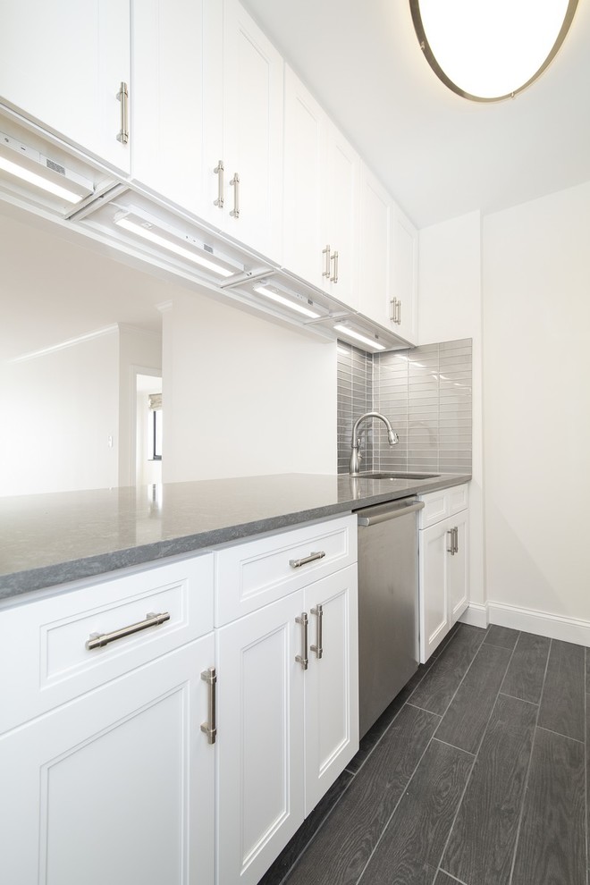Mid-sized transitional galley dark wood floor and gray floor enclosed kitchen photo in New York with an undermount sink, recessed-panel cabinets, white cabinets, quartz countertops, gray backsplash, glass tile backsplash, stainless steel appliances, no island and gray countertops