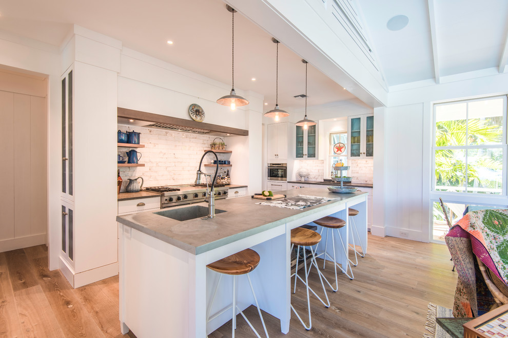 Design ideas for a mid-sized eclectic u-shaped open plan kitchen in Tampa with an undermount sink, shaker cabinets, white cabinets, limestone benchtops, white splashback, subway tile splashback, panelled appliances, light hardwood floors, with island, beige floor and grey benchtop.