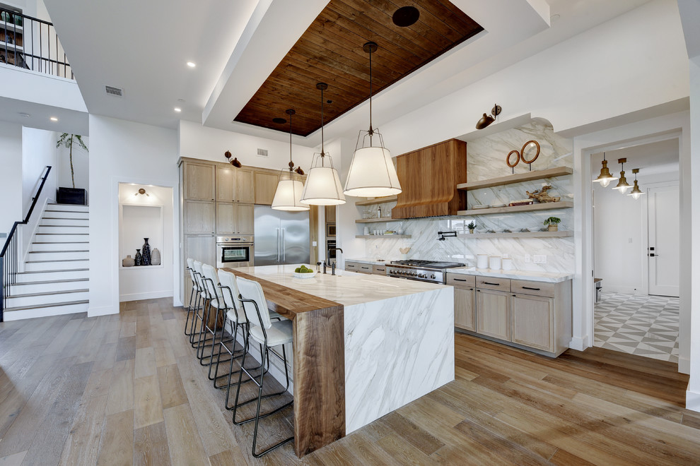 Design ideas for a contemporary l-shaped kitchen in Austin with a farmhouse sink, shaker cabinets, light wood cabinets, white splashback, stainless steel appliances, medium hardwood floors, with island, brown floor and white benchtop.