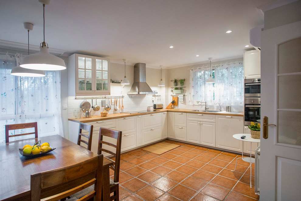 Design ideas for a mid-sized country l-shaped eat-in kitchen in Valencia with recessed-panel cabinets, white cabinets, wood benchtops, white splashback, terra-cotta floors and no island.