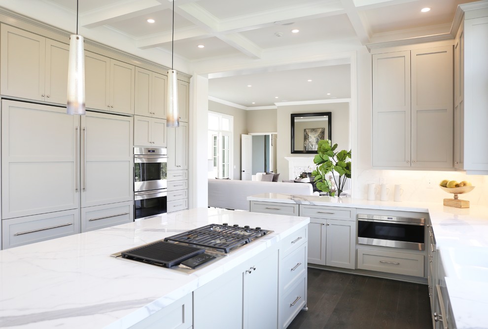 Large traditional l-shaped kitchen in Los Angeles with a farmhouse sink, shaker cabinets, beige cabinets, marble benchtops, white splashback, stone slab splashback, stainless steel appliances, dark hardwood floors and with island.