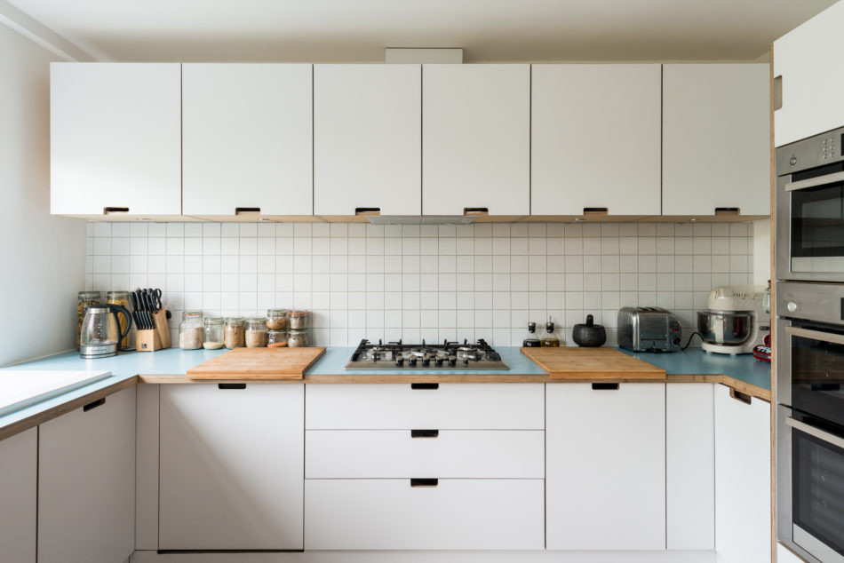 Mid-sized midcentury u-shaped eat-in kitchen in London with a double-bowl sink, flat-panel cabinets, white cabinets, wood benchtops, white splashback, cement tile splashback, stainless steel appliances, medium hardwood floors, no island, brown floor and blue benchtop.