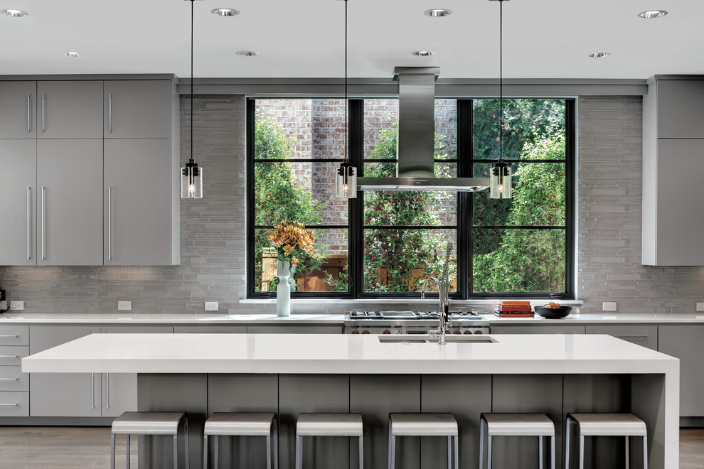 Design ideas for a large modern single-wall eat-in kitchen in Chicago with an undermount sink, flat-panel cabinets, grey cabinets, solid surface benchtops, grey splashback, matchstick tile splashback, stainless steel appliances, light hardwood floors and with island.