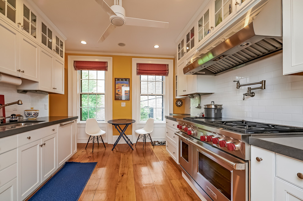 Example of a mid-sized transitional u-shaped medium tone wood floor and beige floor enclosed kitchen design in Boston with an undermount sink, shaker cabinets, white cabinets, solid surface countertops, white backsplash, subway tile backsplash, stainless steel appliances and no island