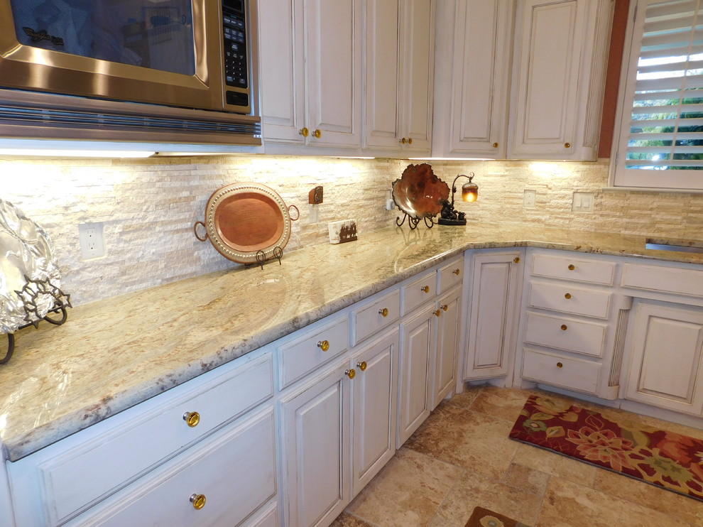This is an example of a mid-sized mediterranean l-shaped eat-in kitchen in Dallas with an undermount sink, raised-panel cabinets, white cabinets, granite benchtops, white splashback, stone tile splashback, stainless steel appliances, porcelain floors and with island.