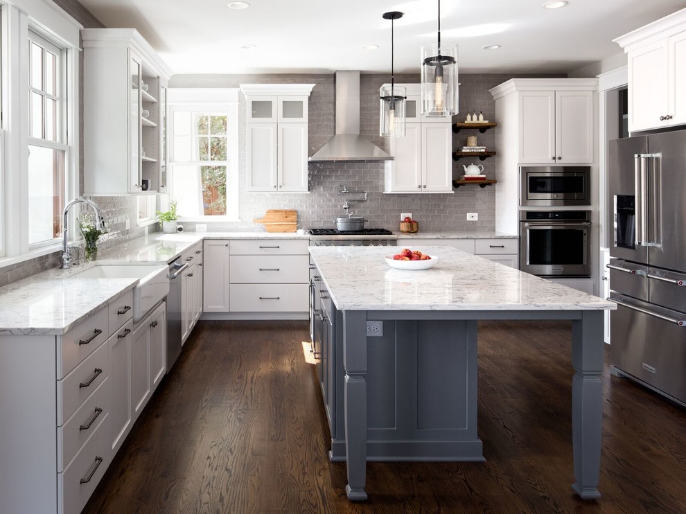 Elegant l-shaped dark wood floor and brown floor kitchen photo in DC Metro with a farmhouse sink, shaker cabinets, white cabinets, gray backsplash, glass tile backsplash, stainless steel appliances and an island