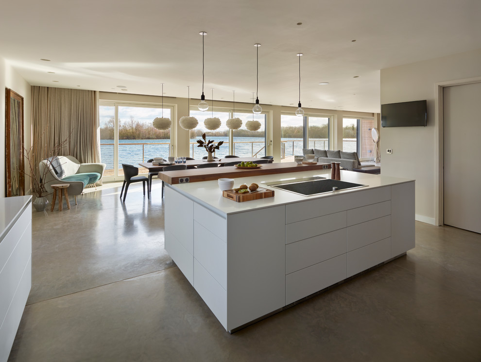 This is an example of a large contemporary l-shaped open plan kitchen in Gloucestershire with flat-panel cabinets, white cabinets, quartz benchtops, stainless steel appliances, concrete floors and with island.