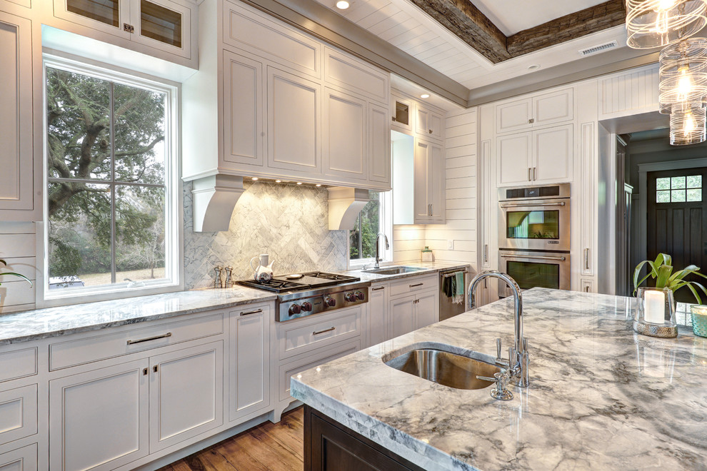 Photo of a mid-sized beach style u-shaped eat-in kitchen in Charleston with an undermount sink, flat-panel cabinets, white cabinets, white splashback, stone tile splashback, stainless steel appliances, medium hardwood floors and with island.