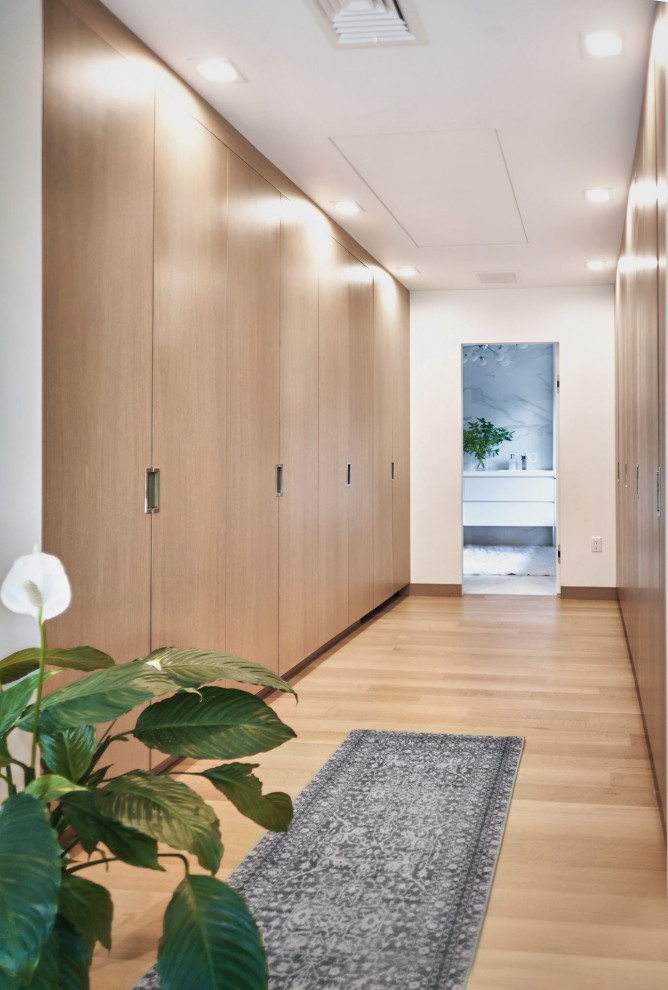 Mid-sized contemporary gender-neutral storage and wardrobe in New York with flat-panel cabinets, light wood cabinets, light hardwood floors and beige floor.