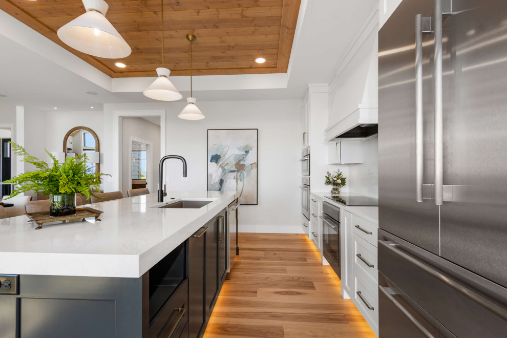 Eat-in kitchen - mid-sized transitional single-wall medium tone wood floor, brown floor and tray ceiling eat-in kitchen idea with an undermount sink, shaker cabinets, white cabinets, quartz countertops, white backsplash, quartz backsplash, stainless steel appliances, an island and white countertops