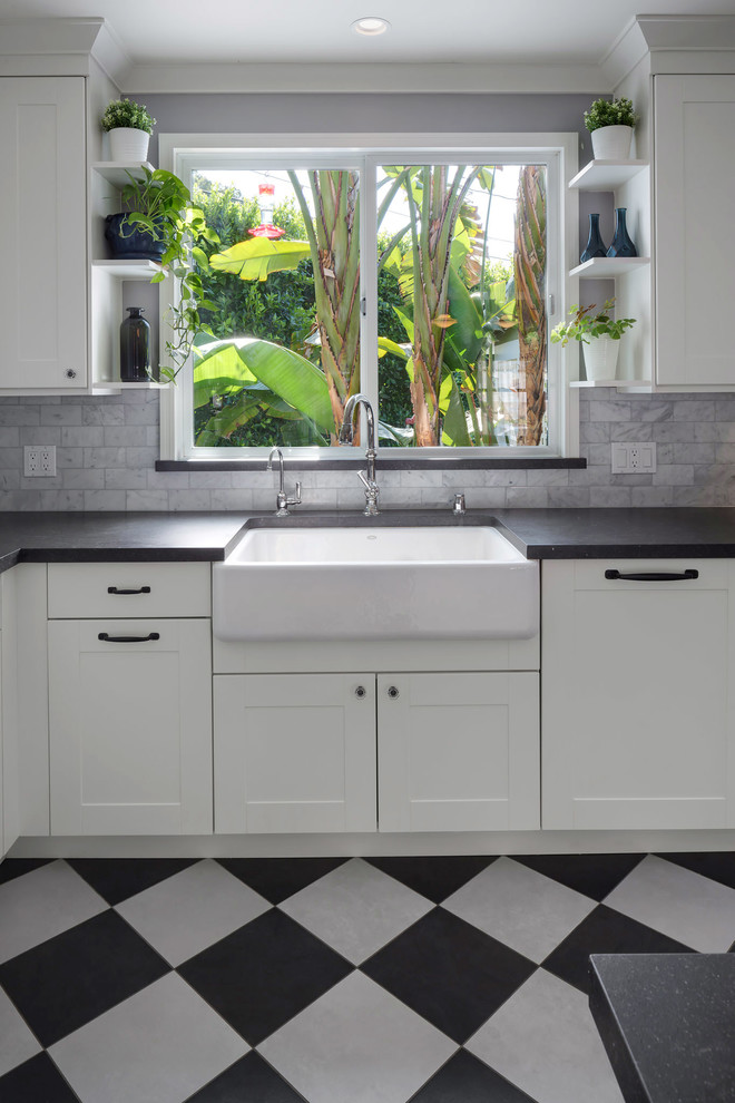 Mid-sized eclectic galley eat-in kitchen with a farmhouse sink, shaker cabinets, white cabinets, quartz benchtops, white splashback, marble splashback, stainless steel appliances, porcelain floors, multi-coloured floor and black benchtop.