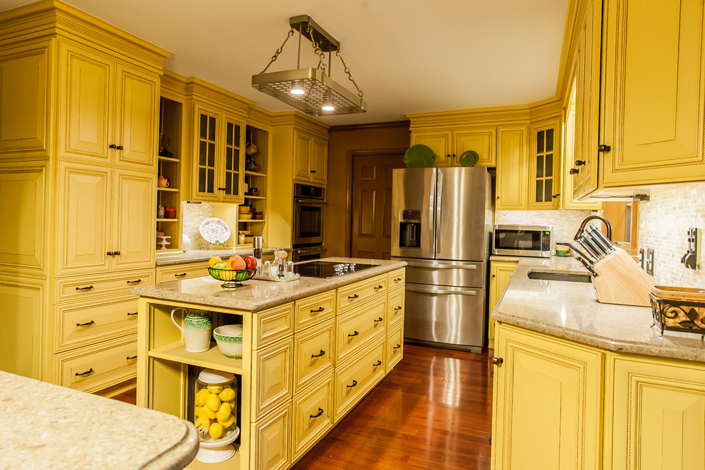 This is an example of a mid-sized country l-shaped separate kitchen in Baltimore with an undermount sink, beaded inset cabinets, yellow cabinets, quartz benchtops, beige splashback, stone tile splashback, stainless steel appliances, medium hardwood floors, with island and brown floor.