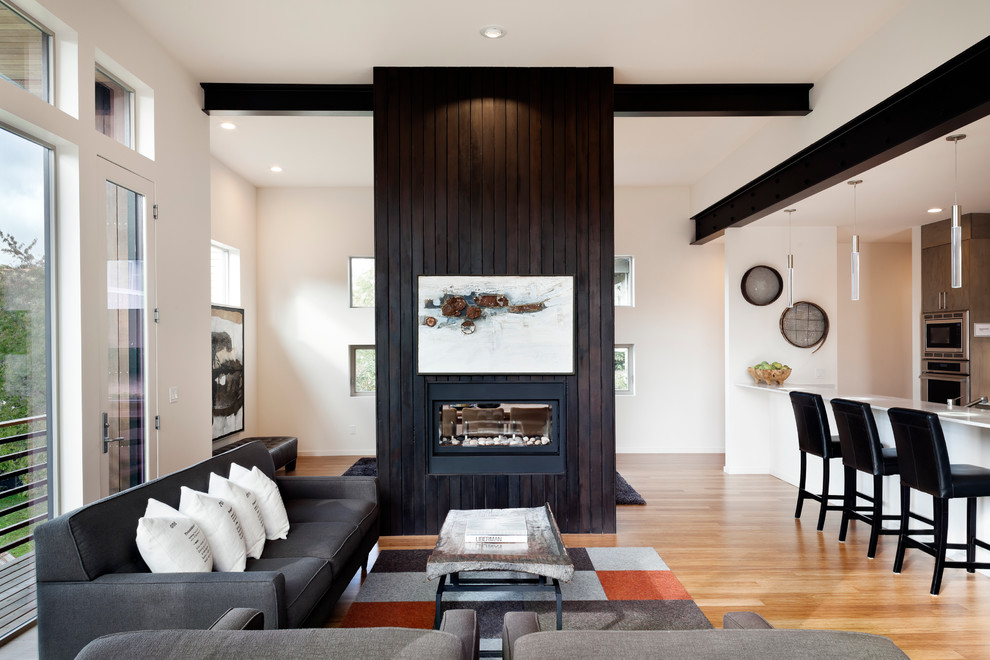 This is an example of a mid-sized modern loft-style living room in Seattle with bamboo floors, a two-sided fireplace and a wood fireplace surround.