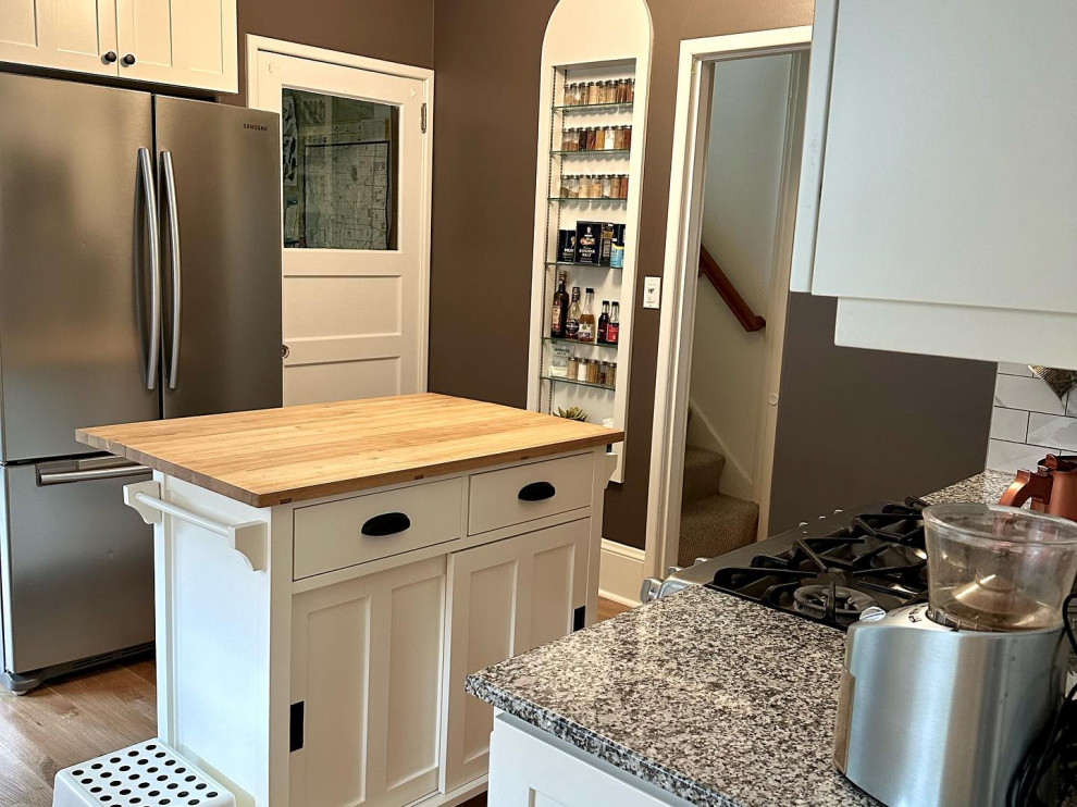 Modelo de cocina comedor de estilo de casa de campo con puertas de armario blancas, salpicadero multicolor, electrodomésticos de acero inoxidable y una isla