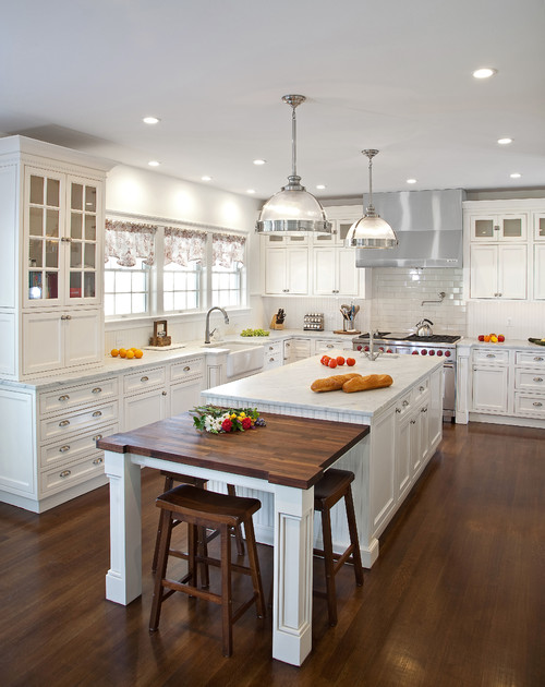 Bright traditional kitchen with white kitchen cabinet wall, large island, and wood table extension on hardwood floors.