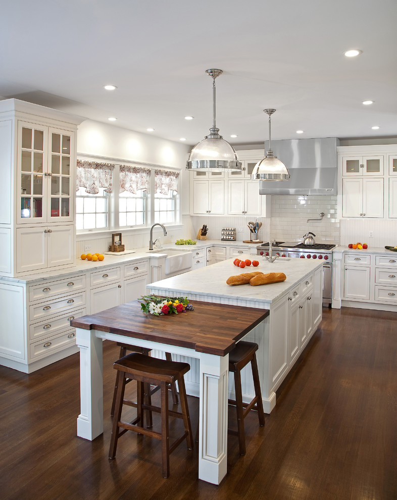 This is an example of a mid-sized traditional kitchen in New York with a farmhouse sink, beaded inset cabinets, white cabinets, marble benchtops, white splashback, subway tile splashback, stainless steel appliances, dark hardwood floors, with island and white benchtop.