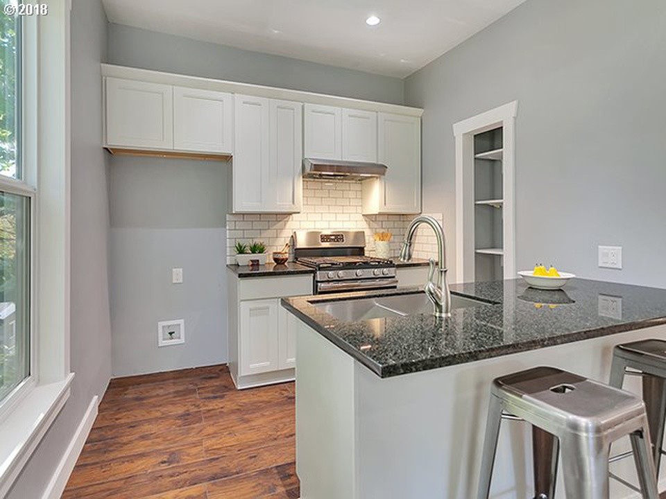 This is an example of a small arts and crafts galley eat-in kitchen in Portland with a double-bowl sink, recessed-panel cabinets, white cabinets, granite benchtops, grey splashback, subway tile splashback, stainless steel appliances, medium hardwood floors, a peninsula, brown floor and grey benchtop.