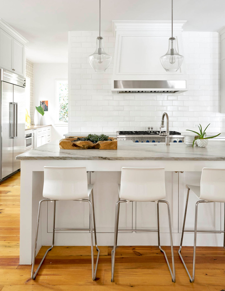 Photo of a country kitchen in Dallas with white cabinets, white splashback, subway tile splashback, stainless steel appliances, medium hardwood floors and with island.