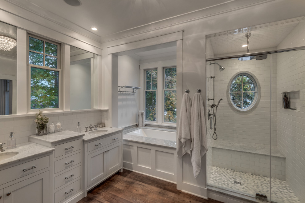 Photo of a classic ensuite bathroom in Boston with shaker cabinets, white cabinets, a submerged bath, an alcove shower, white tiles, metro tiles, white walls, dark hardwood flooring, a submerged sink, brown floors, a hinged door, white worktops, a shower bench, double sinks and a built in vanity unit.