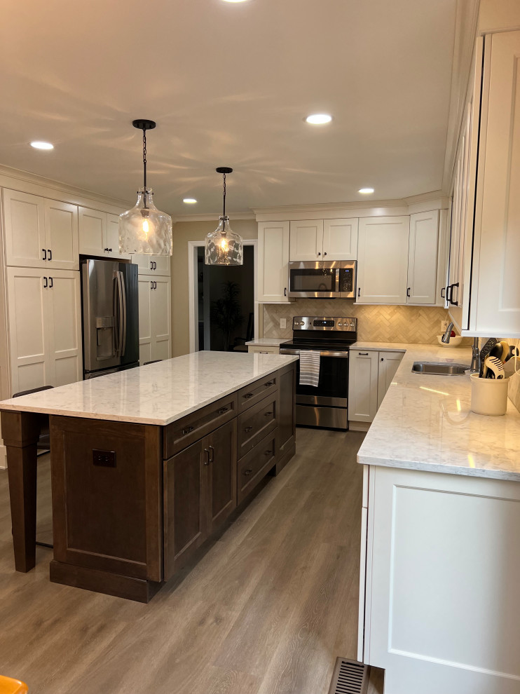 Inspiration for a mid-sized transitional l-shaped laminate floor and brown floor kitchen pantry remodel in Cincinnati with an undermount sink, recessed-panel cabinets, white cabinets, quartz countertops, gray backsplash, stone tile backsplash, stainless steel appliances, an island and white countertops