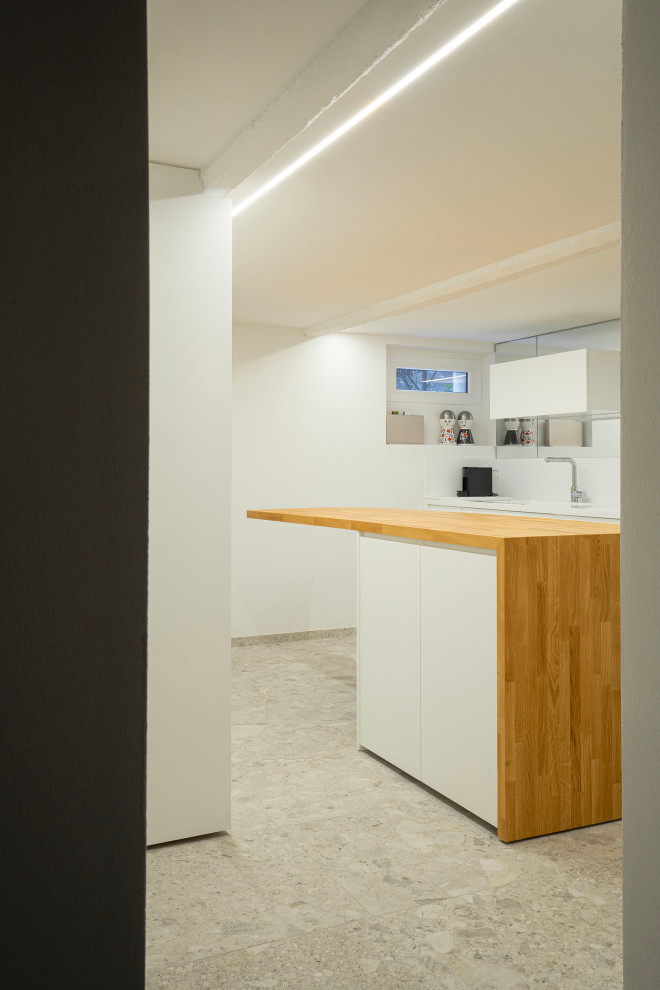 This is an example of a small modern galley open plan kitchen in Milan with an integrated sink, glass-front cabinets, white cabinets, solid surface benchtops, white splashback, mirror splashback, black appliances, with island, beige floor, white benchtop and exposed beam.