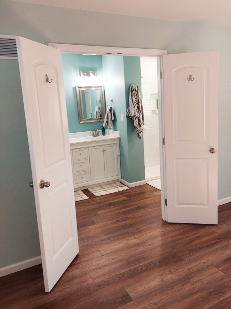 На фото: большая главная ванная комната в стиле модернизм с белыми фасадами, душем без бортиков, унитазом-моноблоком, белой плиткой, плиткой из сланца, синими стенами, полом из ламината, накладной раковиной, столешницей из искусственного кварца, коричневым полом, душем с распашными дверями, белой столешницей, сиденьем для душа, тумбой под две раковины и встроенной тумбой с