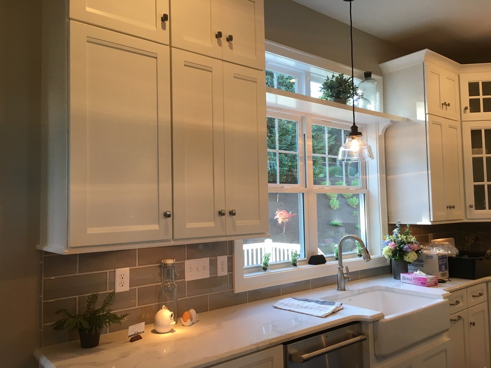 Inspiration for a mid-sized transitional u-shaped kitchen remodel with a farmhouse sink, recessed-panel cabinets, white cabinets, quartz countertops, gray backsplash, ceramic backsplash, stainless steel appliances and white countertops