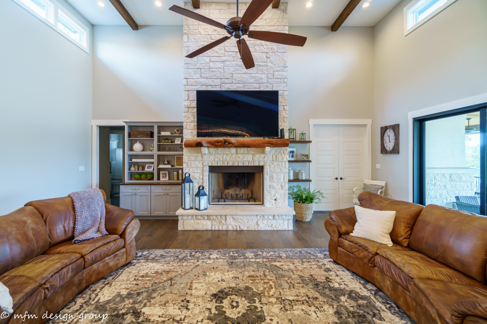 Inspiration for a large contemporary open concept dark wood floor, brown floor and exposed beam living room remodel in Austin with beige walls, a standard fireplace, a stone fireplace and a wall-mounted tv