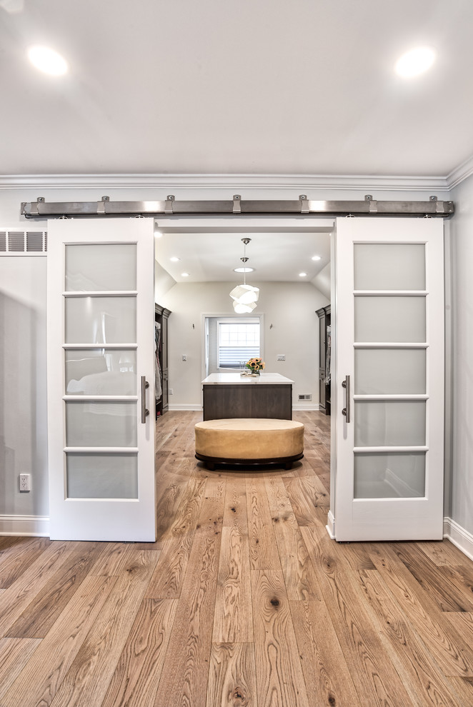 Inspiration for an expansive transitional gender-neutral walk-in wardrobe in New York with dark wood cabinets, light hardwood floors and flat-panel cabinets.