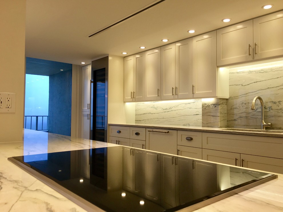 Inspiration for a large transitional galley light wood floor and beige floor open concept kitchen remodel in Miami with an undermount sink, shaker cabinets, white cabinets, marble countertops, gray backsplash, marble backsplash, stainless steel appliances and an island