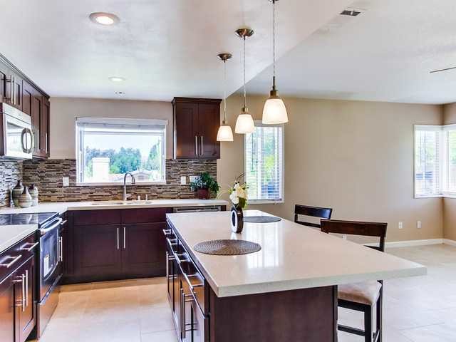 Photo of a mid-sized transitional l-shaped eat-in kitchen in San Diego with an undermount sink, shaker cabinets, dark wood cabinets, quartz benchtops, multi-coloured splashback, matchstick tile splashback, stainless steel appliances, porcelain floors and with island.