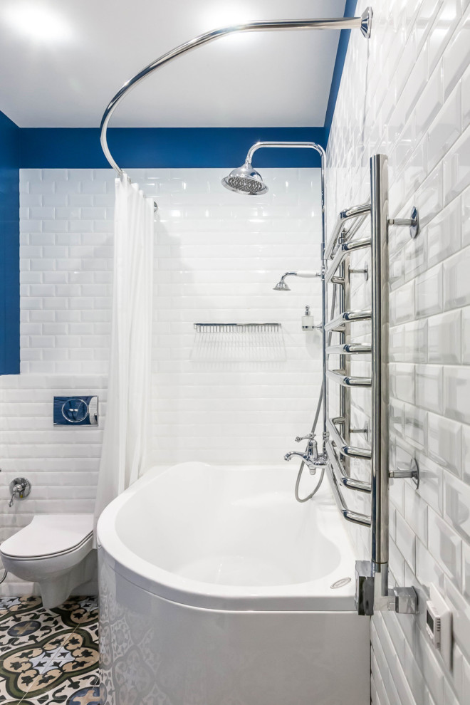Photo of a mid-sized transitional master bathroom in Moscow with louvered cabinets, blue cabinets, a corner tub, a shower/bathtub combo, a wall-mount toilet, white tile, ceramic tile, blue walls, porcelain floors, multi-coloured floor and a shower curtain.