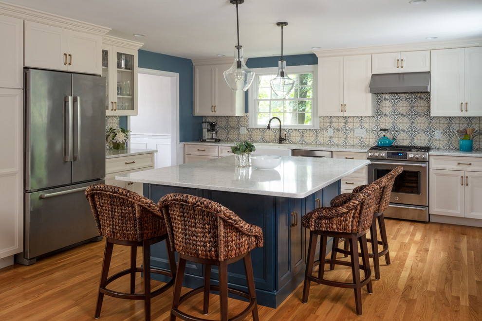 Photo of a beach style kitchen in Boston with a farmhouse sink, recessed-panel cabinets, beige cabinets, multi-coloured splashback, stainless steel appliances, medium hardwood floors, with island and grey benchtop.