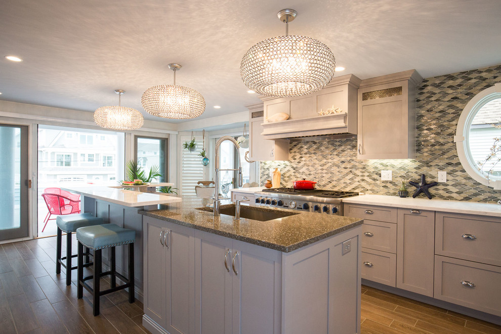 Mid-sized beach style l-shaped medium tone wood floor and beige floor open concept kitchen photo in Boston with shaker cabinets, gray cabinets, granite countertops, multicolored backsplash, stone tile backsplash, stainless steel appliances and an island