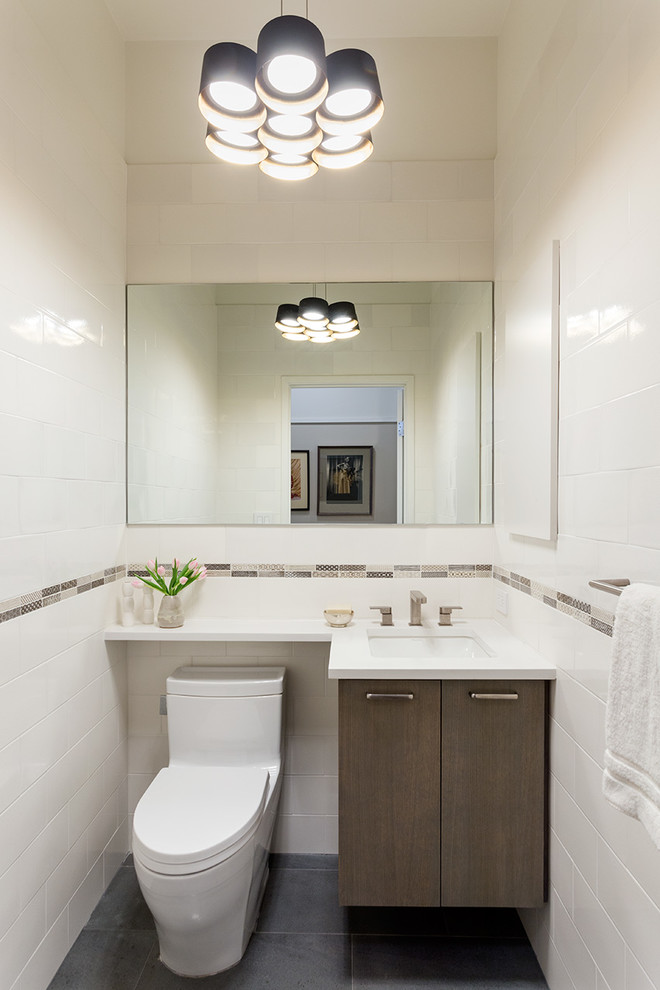 Photo of a small contemporary powder room in New York with flat-panel cabinets, medium wood cabinets, engineered quartz benchtops, a one-piece toilet, ceramic tile, white walls, ceramic floors, an undermount sink and white tile.
