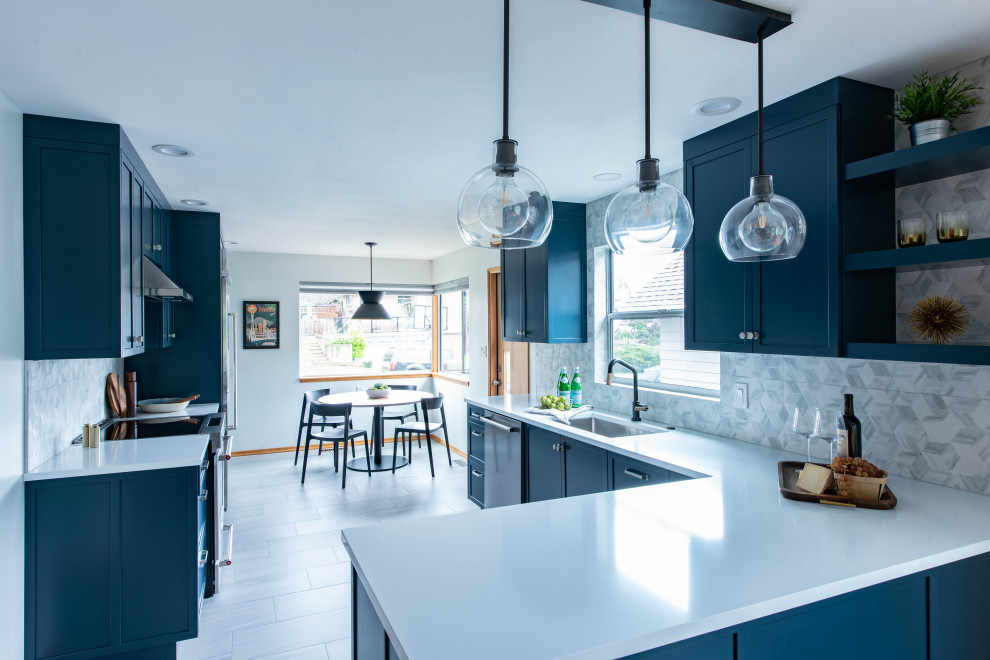 This is an example of a mid-sized midcentury u-shaped eat-in kitchen in Seattle with an undermount sink, recessed-panel cabinets, blue cabinets, quartz benchtops, grey splashback, porcelain splashback, stainless steel appliances, porcelain floors, a peninsula, grey floor and white benchtop.