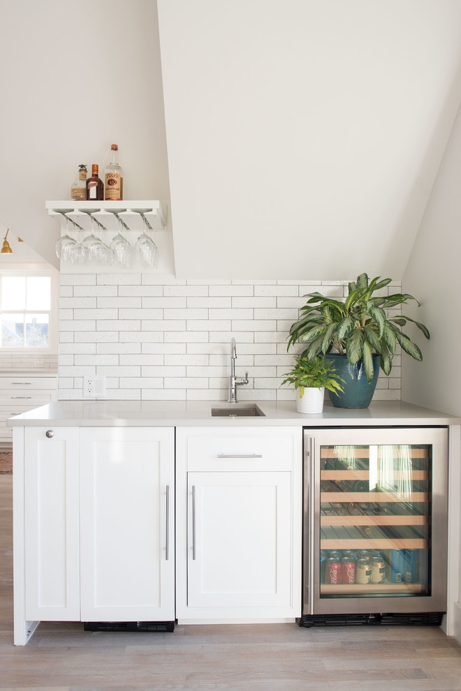 Small beach style single-wall wet bar in Boston with an undermount sink, shaker cabinets, white cabinets, white splashback, subway tile splashback, light hardwood floors, beige floor, grey benchtop and quartz benchtops.