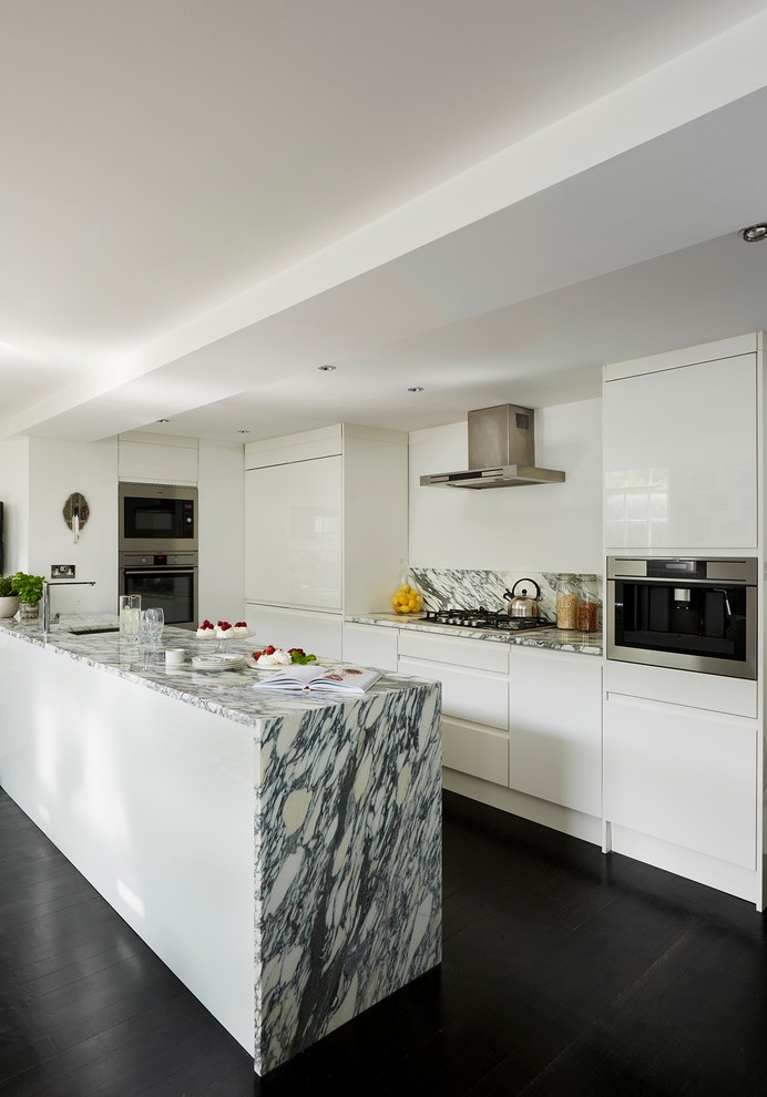 Photo of a contemporary galley kitchen in London with an undermount sink, flat-panel cabinets, white cabinets, stainless steel appliances, dark hardwood floors and with island.