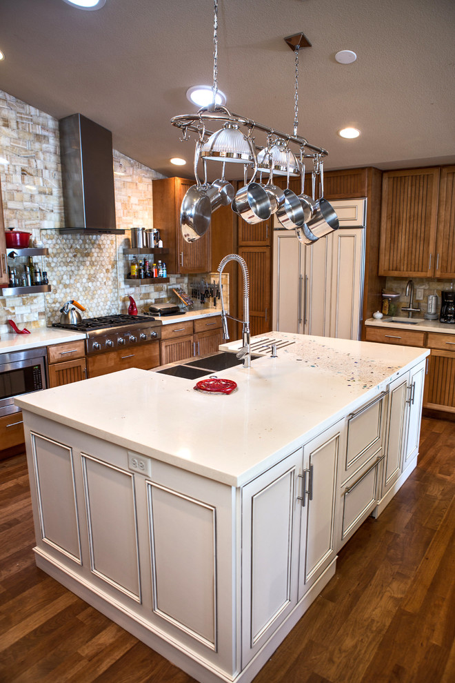 This is an example of a large transitional l-shaped kitchen in Denver with a farmhouse sink, louvered cabinets, medium wood cabinets, quartzite benchtops, beige splashback, stone tile splashback, panelled appliances, dark hardwood floors, multiple islands, brown floor and white benchtop.