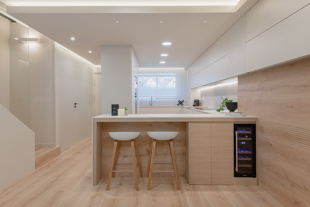Inspiration for a mid-sized contemporary u-shaped kitchen in Other with flat-panel cabinets, white cabinets, white splashback, panelled appliances, light hardwood floors, a peninsula, beige floor and white benchtop.