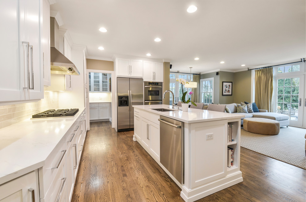 Example of a mid-sized transitional single-wall medium tone wood floor open concept kitchen design in Chicago with an undermount sink, shaker cabinets, white cabinets, quartz countertops, gray backsplash, ceramic backsplash, stainless steel appliances, an island and white countertops
