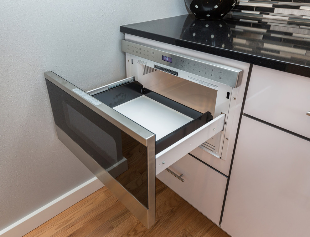 Open concept kitchen - large contemporary u-shaped light wood floor open concept kitchen idea with an undermount sink, flat-panel cabinets, white cabinets, granite countertops, multicolored backsplash, mosaic tile backsplash, stainless steel appliances and an island